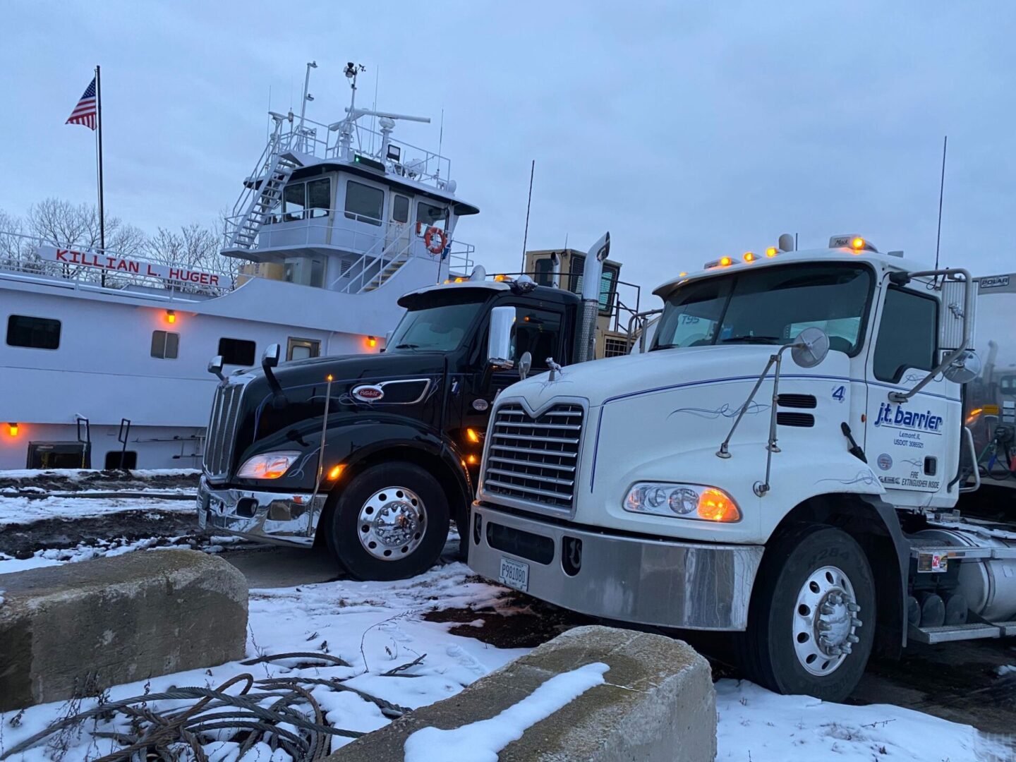 Two semi trucks parked in front of a boat.