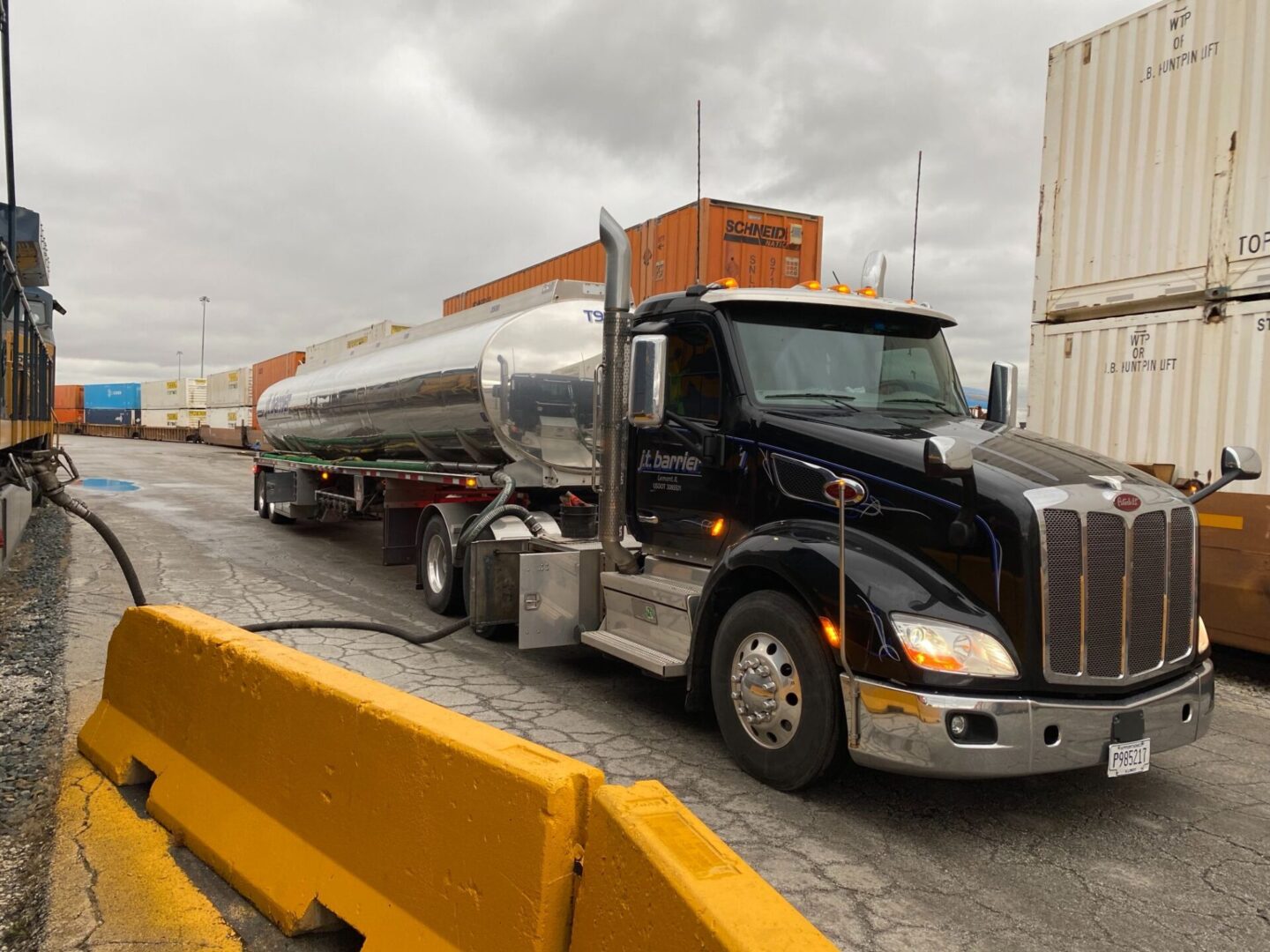 A black semi truck is parked next to a container.